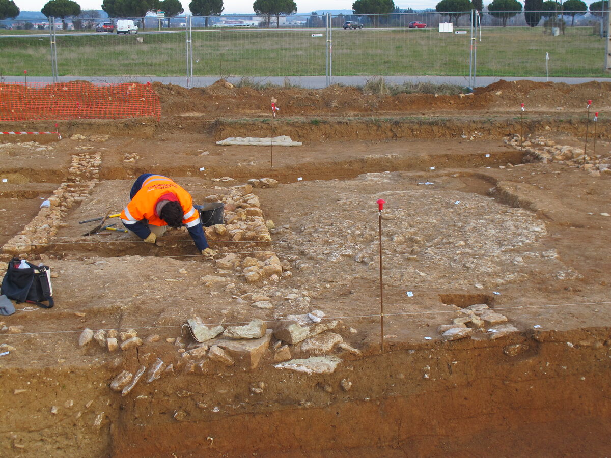 Inrap archaeologists excavating a stripped surface, crouching over structures revealed in the ground